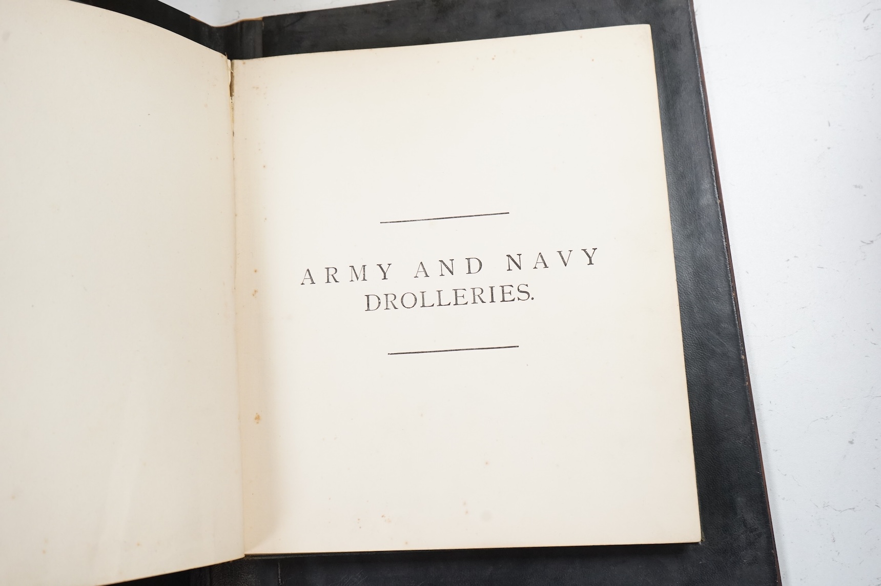 An olive and marquetry desk blotter, Duke of Wellington on horseback and his coat of arms, together with a cloth and gilt book, Army and Navy Drolleries by Captain Seccombe